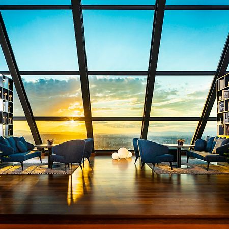 Grand Hotel Millennium صوفيا المظهر الخارجي الصورة The photo depicts a modern, stylish interior of a high-rise space with a panoramic view through large glass windows. The scene features a cozy seating area with several blue armchairs arranged around a low table, creating a comfortable atmosphere. Th