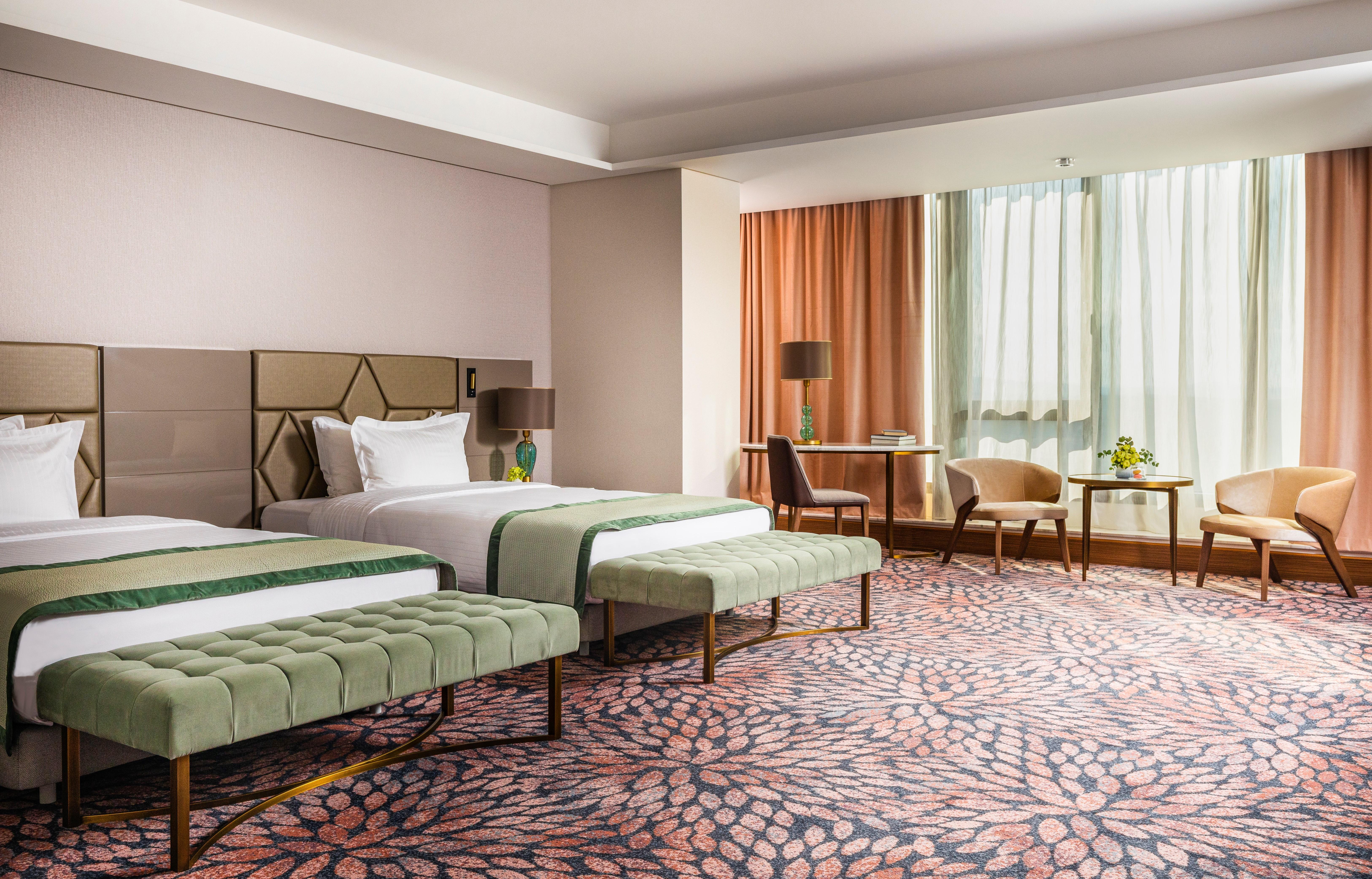 Grand Hotel Millennium صوفيا المظهر الخارجي الصورة The image shows a well-decorated hotel room featuring two beds with green striped bedspreads. There is a plush green bench at the foot of each bed. The room has large windows with sheer curtains allowing natural light to enter. There is a cozy seatin