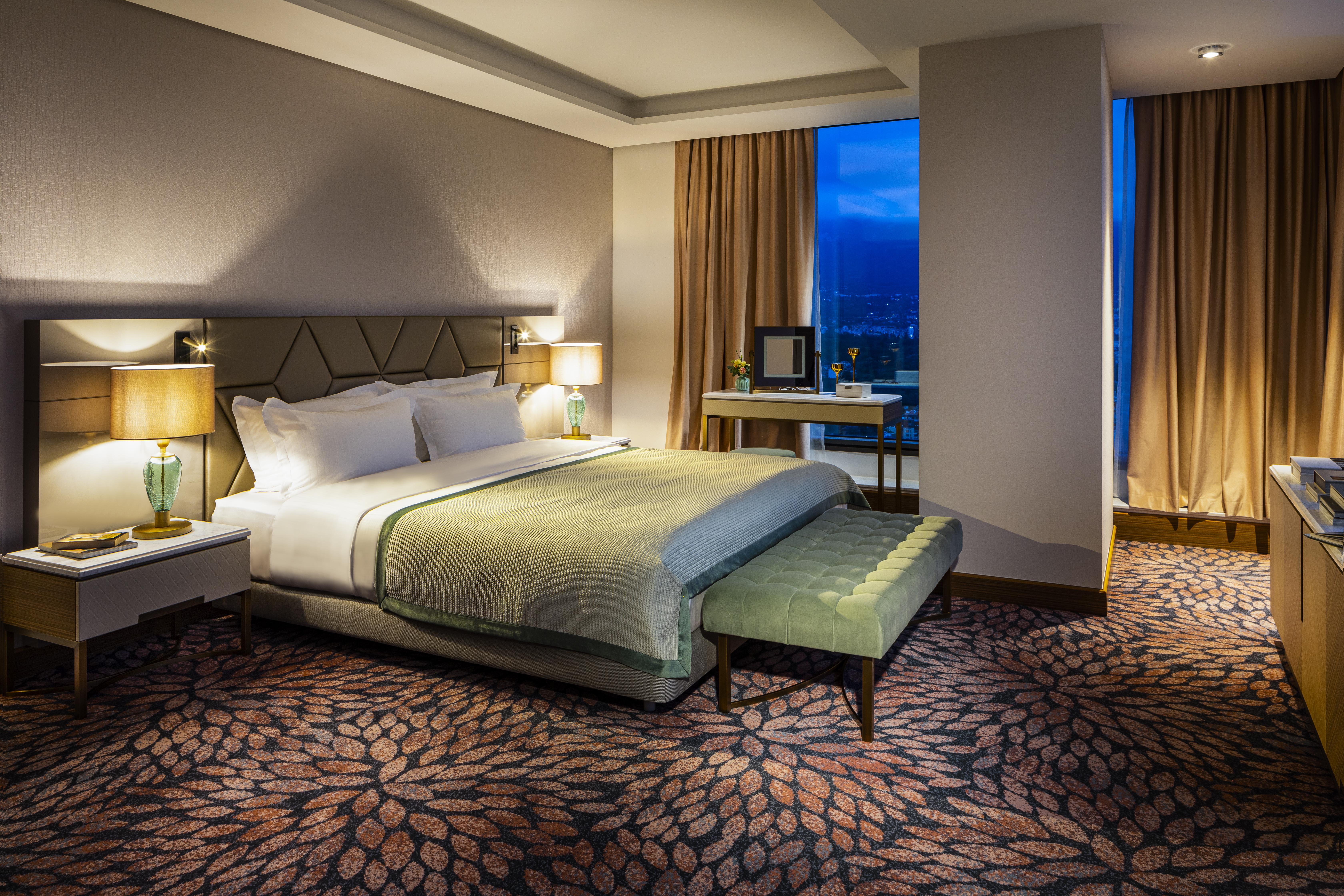 Grand Hotel Millennium صوفيا المظهر الخارجي الصورة The photo shows a modern hotel room featuring a spacious design. It has a large bed with a light green throw blanket positioned in the center. On either side of the bed, there are stylish bedside tables with lamps. 

The floor has a patterned carpet,
