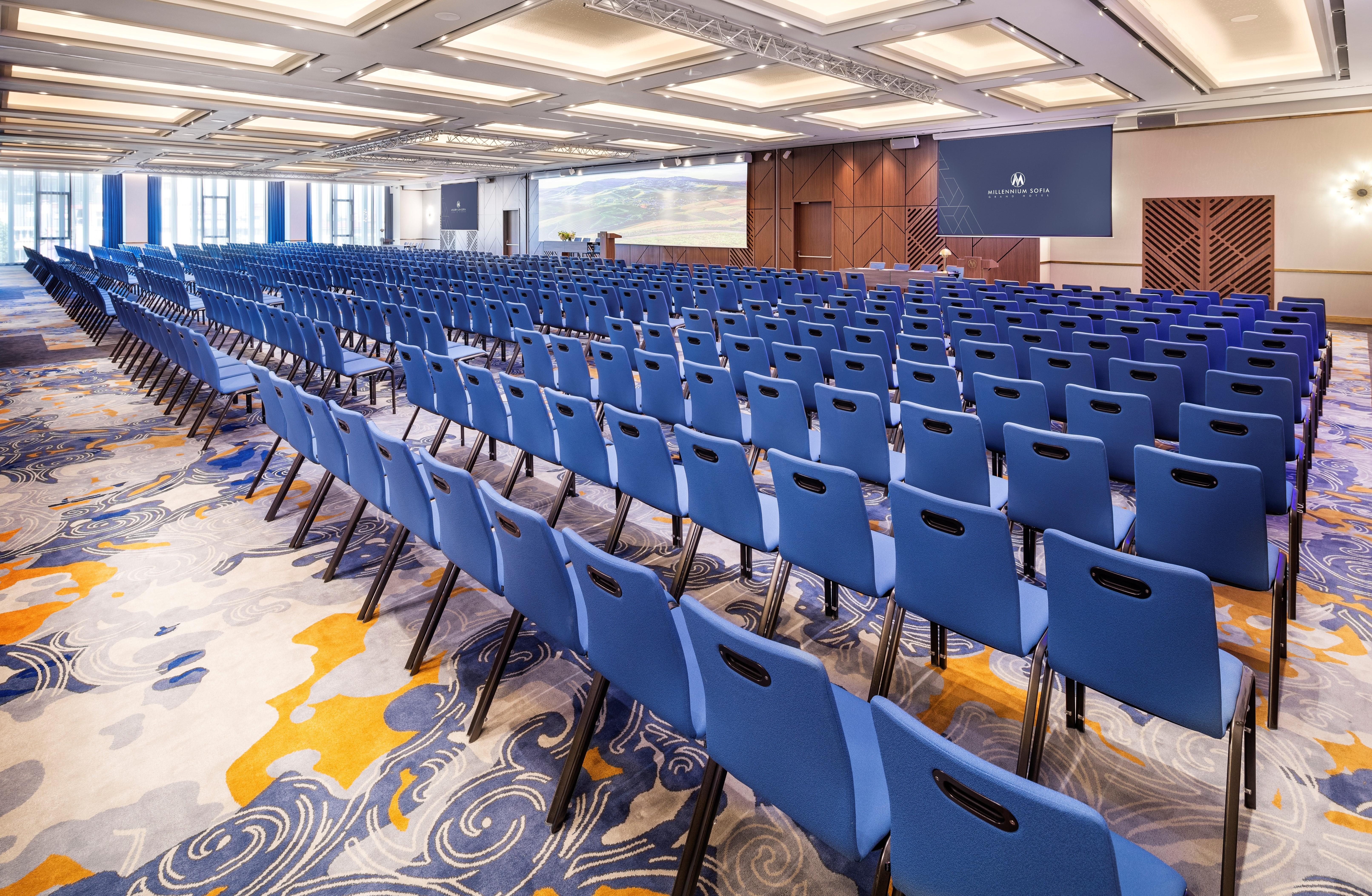 Grand Hotel Millennium صوفيا المظهر الخارجي الصورة The photo shows a large conference or meeting room set up for an event. There are numerous blue chairs arranged in rows, creating a seating area for attendees. The floor features a decorative pattern, and the room has a modern design with ample light