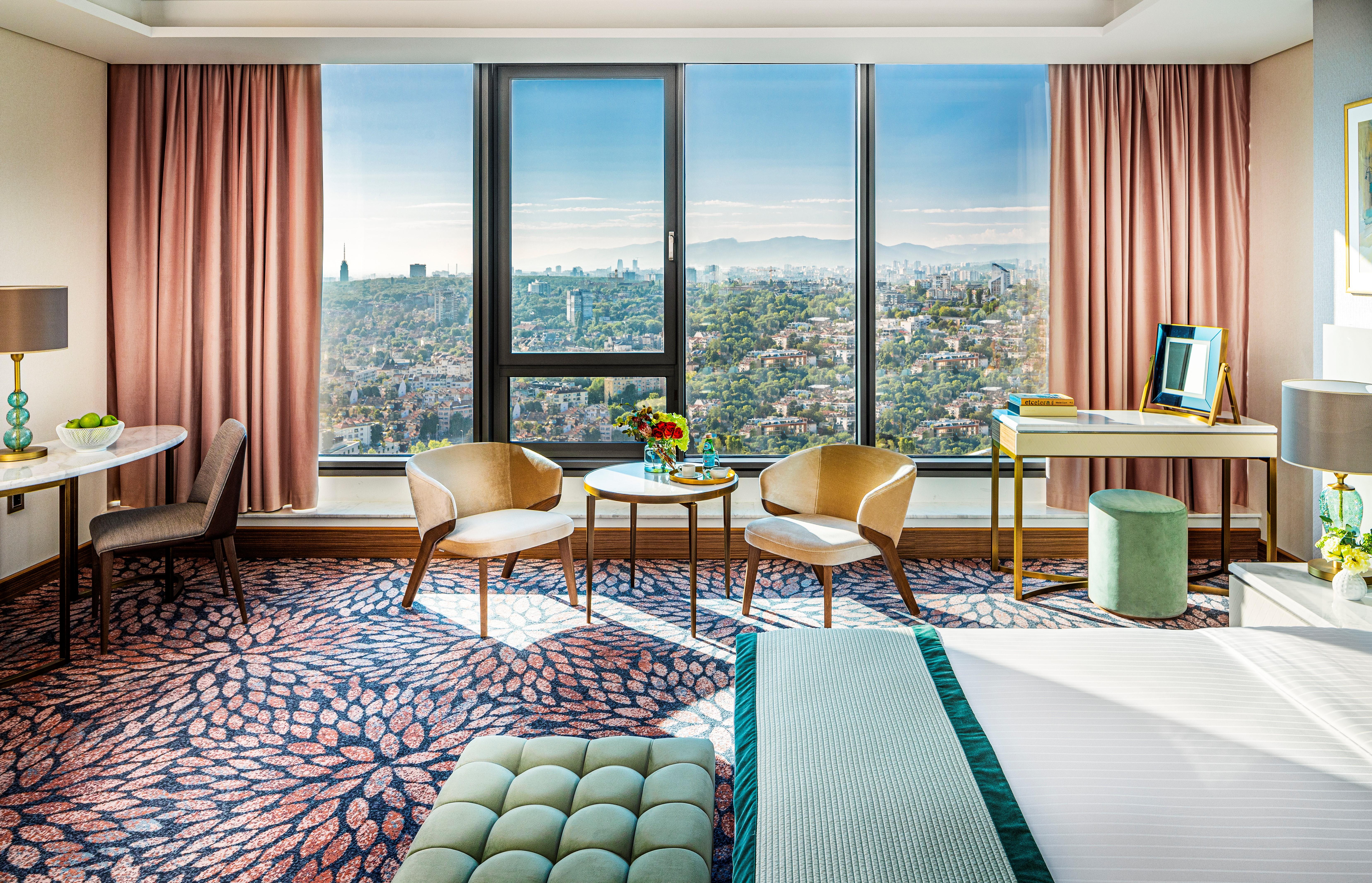Grand Hotel Millennium صوفيا المظهر الخارجي الصورة The photo shows a stylish hotel room featuring modern decor. There are large windows that offer a panoramic view of the cityscape, allowing natural light to fill the space. The walls are adorned with soft pink curtains. In the room, there are two ele