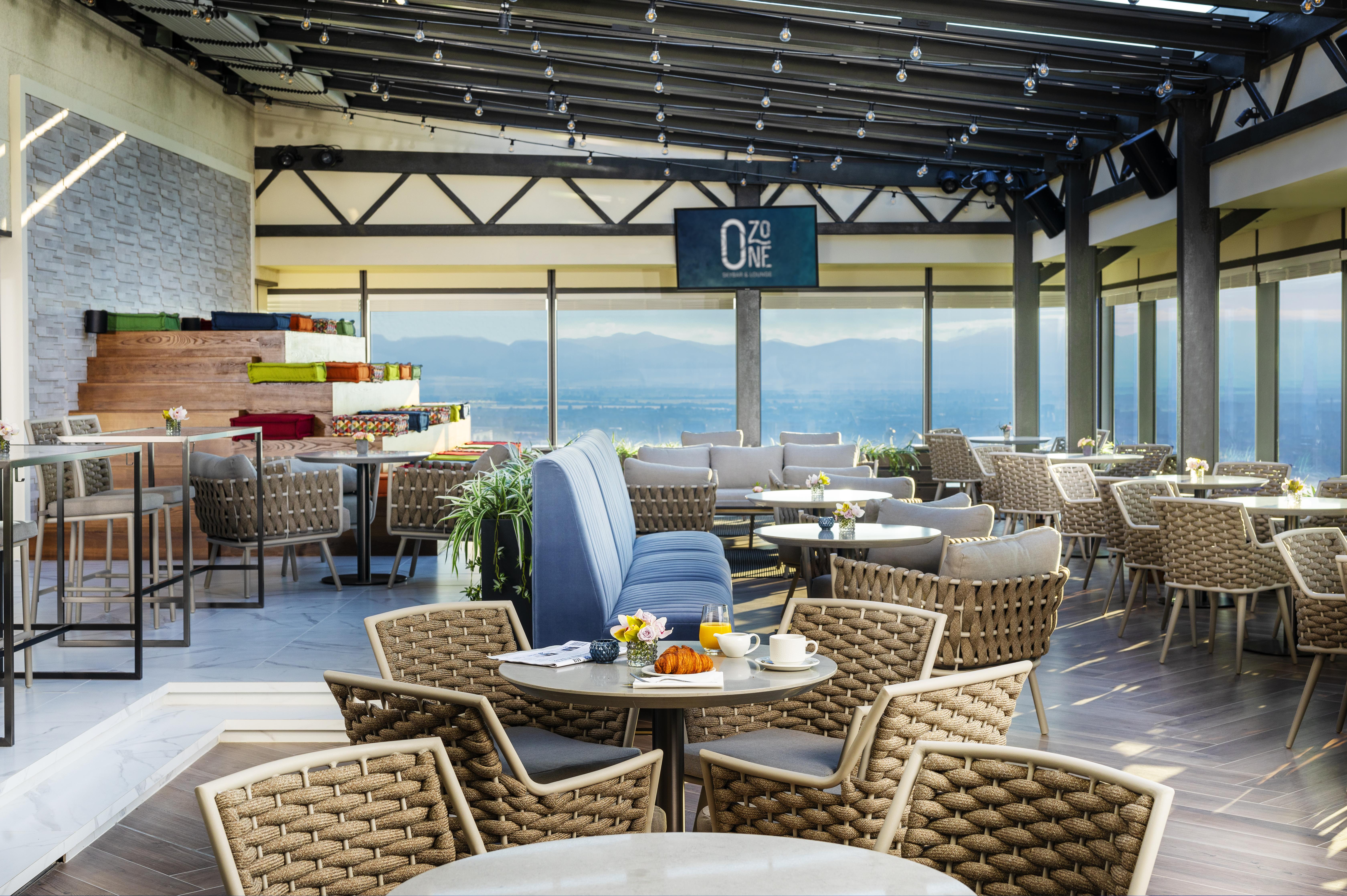 Grand Hotel Millennium صوفيا المظهر الخارجي الصورة The photo shows a modern restaurant or café with a spacious interior. It features a variety of seating arrangements, including round tables surrounded by wicker chairs and lounges. Large windows allow for a panoramic view, which likely includes sceni